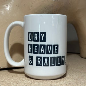 May include: White ceramic mug with black lettering that reads "DRY HEAVE & RALLY".