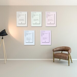 Op de afbeelding: Vijf ingelijste kunstdrukken met tekst en veerillustraties hangen aan een muur. De prints hebben verschillende pastelkleurige achtergronden: lichtgroen, roze en blauw. Een moderne vloerlamp en een bruine leren fauteuil staan ook in de kamer.