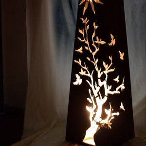 Könnte beinhalten: Eine schwarze Metalllampe mit einem ausgeschnittenen Design eines Baumes und Vögeln. Die Lampe wird von innen beleuchtet und erzeugt ein warmes Leuchten.