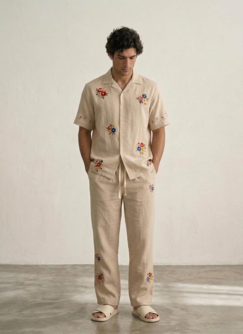 Puede incluir: Conjunto de camisa y pantal&oacute;n de lino beige con bordados florales coloridos. La camisa de manga corta tiene cuello de solapa y el pantal&oacute;n tiene cintura con cord&oacute;n. El conjunto se completa con sandalias blancas, creando un look relajado y casual.