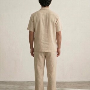 Puede incluir: Un conjunto de camisa y pantal&oacute;n de lino beige. La camisa de manga corta tiene cuello y el pantal&oacute;n es recto. El conjunto est&aacute; hecho de una tela ligera y transpirable, perfecto para el clima c&aacute;lido. El modelo se ve desde atr&aacute;s.