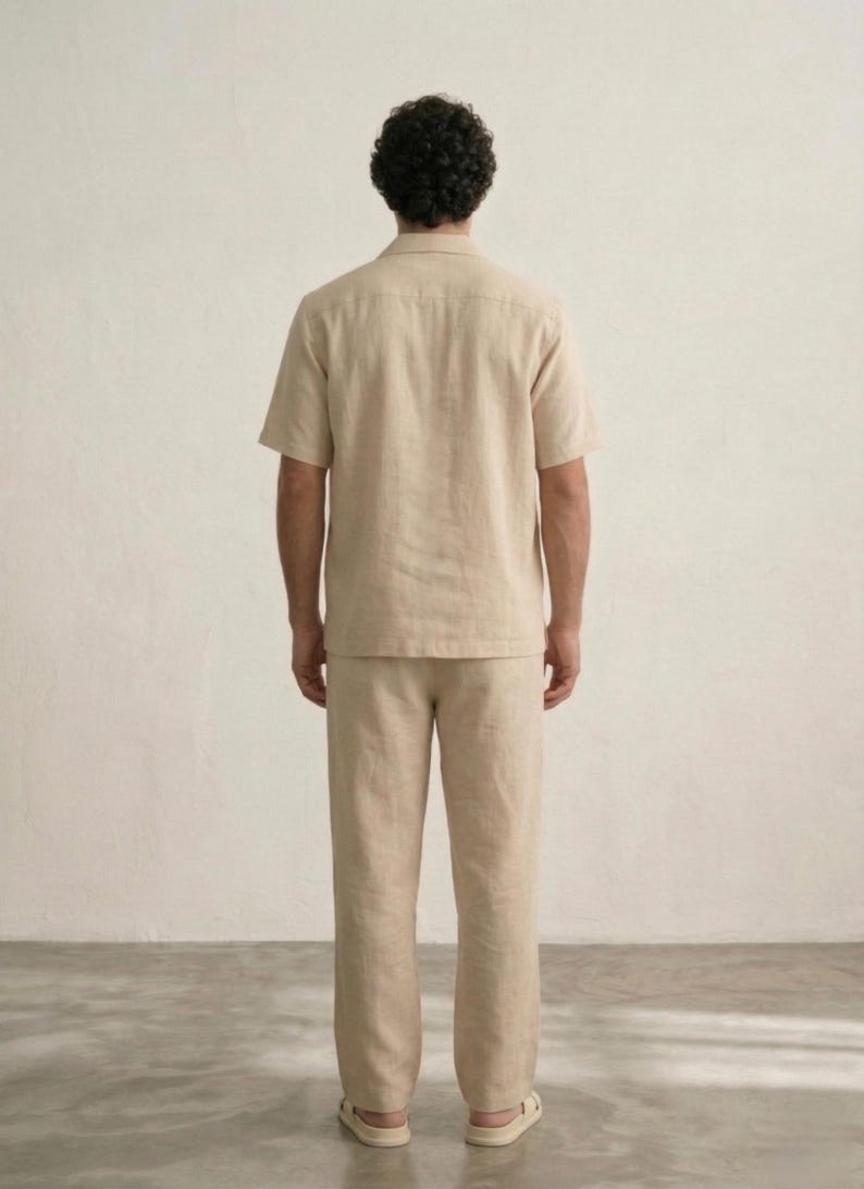 Puede incluir: Un conjunto de camisa y pantal&oacute;n de lino beige. La camisa de manga corta tiene cuello y el pantal&oacute;n es recto. El conjunto est&aacute; hecho de una tela ligera y transpirable, perfecto para el clima c&aacute;lido. El modelo se ve desde atr&aacute;s.