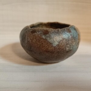 May include: A small, brown and blue ceramic pot with an uneven, textured surface.