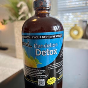 Puede incluir: Una botella de vidrio marrón con tapa negra y etiqueta azul. La etiqueta dice "Dandelion Detox" con un gráfico de flor de diente de león. El texto en la etiqueta menciona remedio herbal y beneficios para la salud.