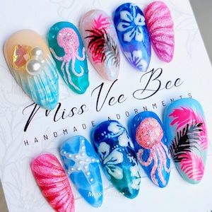 Peut inclure: Ensemble de dix faux ongles colorés avec différents motifs sur le thème de l'été, notamment des coquillages, des étoiles de mer, des méduses et des fleurs tropicales. Les ongles sont étiquetés "Miss Vee Bee Handmade Adornments".