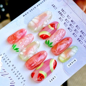 Peut inclure: Un ensemble de faux ongles sur le thème des fruits d'été. Les ongles présentent des motifs de fraises et de pastèques dans des tons de rose, de rouge et de vert. Les ongles sont présentés sur un tableau des tailles.