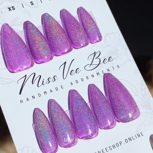 Könnte beinhalten: Ein Set aus lavendelfarbenen, holografischen Press-On-Nägeln. Die Nägel sind mandelförmig und haben ein glitzerndes, irisierendes Finish. Auf der Karte steht "Miss Vee Bee, Handmade Adornments."