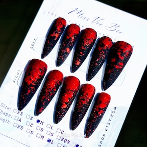 May include: A set of ten long, pointed false nails. Each nail features a black base that fades into a red tip, with a speckled pattern. The text "Miss Vee Bee" and "SHOP.ETSY.COM" are visible.