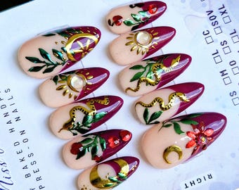 May include: Set of ten burgundy and nude press-on nails with gold and green floral designs, including snakes, moons, and stars. The nails are labeled "LEFT" and "RIGHT".