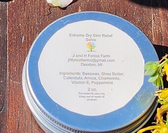 May include: A silver tin with a blue label that reads "Extremo Dry Skin Relief Salve" and lists the ingredients: Beeswax, Shea Butter, Calendula, Arnica, Chamomile, Vitamin E, Peppermint. The label also includes the name of the farm, J and H Forest Farm, the email address, and the location, Deerton, MI. The tin contains 2 oz of salve.