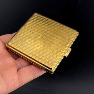 Peut inclure: Un étui à cigarettes en métal doré avec un motif texturé en forme de diamant.