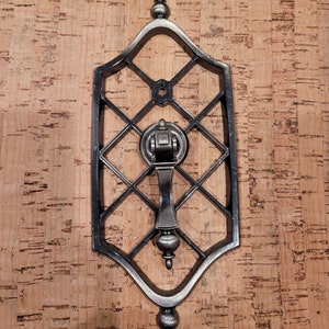 May include: A silver door knocker with a decorative, ornate design. The knocker is attached to a metal frame with a diamond pattern.