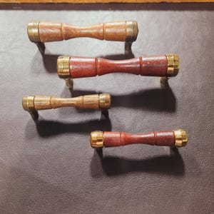 May include: Four wooden drawer pulls with brass accents. The pulls are in different shades of brown and have a simple, elegant design.