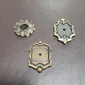 May include: Three ornate metal decorative accents with a hole in the center. The accents are in a gold finish with intricate designs.