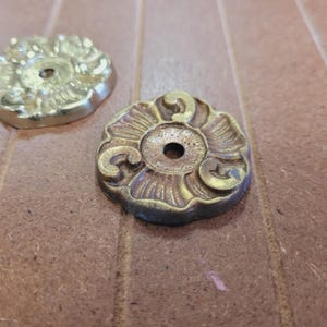 May include: Two ornate brass decorative accents with a circular design and a hole in the center. The accents have a floral pattern and are a gold color.