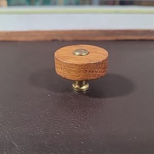 May include: A round wooden knob with a brass center. The knob is a light brown color and has a slightly rough texture.