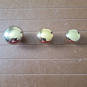 May include: Three gold-toned round cabinet knobs of different sizes.