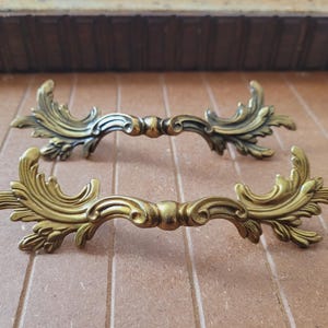 May include: Two ornate gold-toned metal drawer pulls with a leaf design.