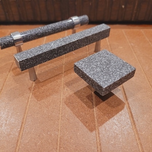 May include: Three cabinet knobs made of gray speckled stone with silver accents. The knobs are in various sizes and shapes.