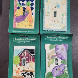 May include: Four decorative light switch covers with hand-painted designs. The designs include a farm scene, a hummingbird with flowers, a fruit and vegetable scene, and a baby theme with the words "New Baby", "Cherished", "Precious", "Adorable", and "Treasured".