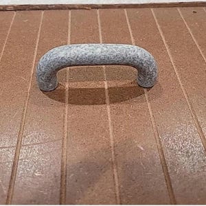 May include: A close-up of a gray metal handle on a wooden surface. The handle is a simple, rounded design with a textured finish.