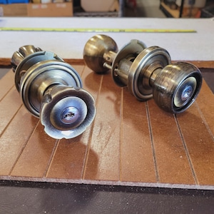 May include: Two antique brass door knobs with keyholes. The knobs are on a wooden surface.