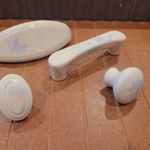 May include: Set of four white ceramic cabinet knobs with a floral design. The knobs feature a raised, embossed floral pattern in shades of blue and pink.