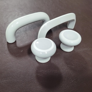 May include: Three white ceramic cabinet knobs with a raised ring around the center. The knobs are on a brown surface.