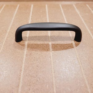 May include: A dark brown, arched cabinet pull handle. The handle is a solid, curved bar with rounded ends, designed for easy gripping. It is made of a matte material and is suitable for drawers or cabinet doors.