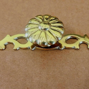 May include: A gold-toned decorative drawer pull with a floral design. The pull has a decorative backplate with a scroll design.