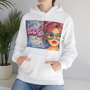 May include: White hooded sweatshirt with a front pocket. The graphic on the front features a mosaic-style illustration of a woman wearing sunglasses with a beach scene reflection, the word "Cool" in pink script, and star accents.