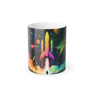 Puede incluir: Taza de cerámica con un diseño de cohete colorido sobre un fondo espacial estrellado. El cohete está representado en tonos de amarillo, naranja y rosa, con una estela de humo y una persona debajo. La taza tiene un interior blanco.