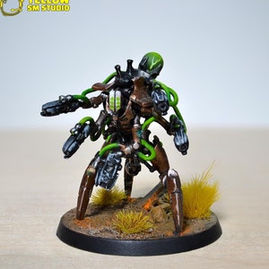 May include: A detailed, hand-painted miniature of a multi-legged robot with green wires and pipes. The robot has multiple guns and a green head. The robot is standing on a brown base with dry brush grass.