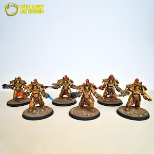 May include: A group of six gold and red painted miniature figures, each holding a weapon, standing on circular bases. The figures are posed in a battle formation.