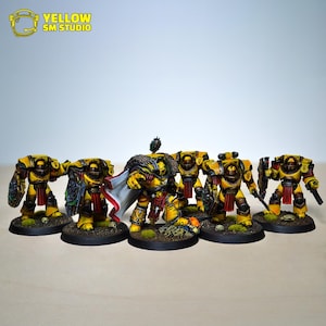 Puede incluir: Un grupo de figuras en miniatura amarillas y rojas, posiblemente para juegos de mesa. Las figuras están blindadas, con armas y escudos. Las bases son oscuras y el fondo es liso.