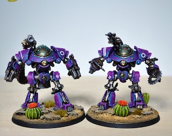 Peut inclure: Deux figurines miniatures de robots violets et bleus, avec des armes détaillées et un emblème de crâne. Les robots sont posés sur une base désertique avec des cactus et de petites plantes. Le texte "YELLOW SM STUDIO" est inclus.
