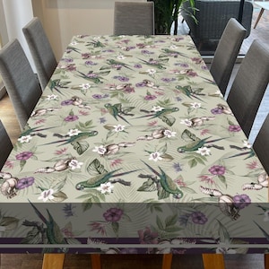 Puede incluir: Un mantel verde con un patrón repetido de loros, flores y hojas. El mantel tiene un borde morado oscuro.