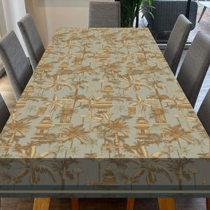 May include: A light blue tablecloth with a repeating pattern of gold palm trees and temples. The tablecloth is laid out on a wooden table with chairs around it.