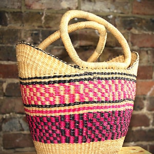 May include: A woven basket with pink, black and natural coloured stripes. The basket has two handles and is made of natural materials.