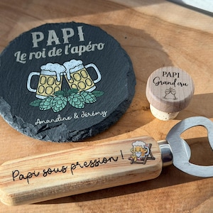 Peut inclure: Un dessous de verre rond en ardoise noire avec le texte PAPI Le roi de l'apéro, un motif de chopes de bière et les noms Amandine & Jérémy. Un bouchon de bouteille en bois marqué PAPI Grand cru et un décapsuleur en bois Papi sous pression.
