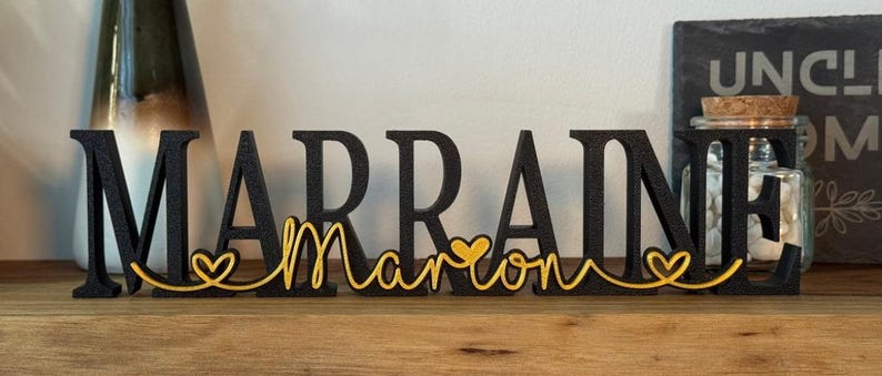 May include: Black wooden letters spelling "MARRAINE" with a gold heart and the word "marron" in gold script.