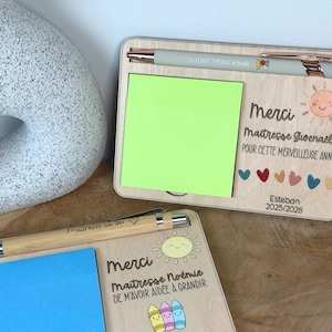 Puede incluir: Dos organizadores de escritorio de madera con bolígrafos, notas adhesivas y texto. Uno tiene una nota adhesiva verde y el texto "Merci Maitresse Gionnaelle POUR CETTE MERVEILLEUSE ANNÉE" y "Esteban 2025/2026". El otro tiene una nota adhesiva azul y el texto "Merci Maitresse Noémie".