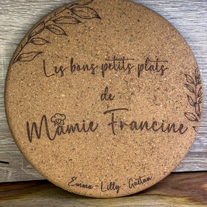 Peut inclure: Un dessous de plat rond en liège avec un motif floral et le texte "Les bons petits plats de Mamie Francine" et les noms "Emma - Lilly - Gaetan" en bas.