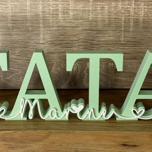 May include: Green wooden letters spelling "TATA" with a white outline of the word "MARINE" and hearts between the letters.