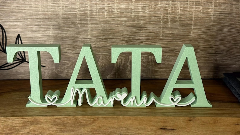 May include: Green wooden letters spelling "TATA" with a white outline of the word "MARINE" and hearts between the letters.