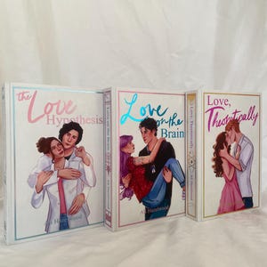 Può includere: Tre libri con copertina rigida con illustrazioni romantiche. I titoli sono "The Love Hypothesis", "Love on the Brain" e "Love, Theoretically". Ogni libro presenta una coppia in un abbraccio romantico, con il nome dell'autore, Ali Hazelwood, visibile.