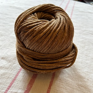 Op de afbeelding: Een bol bruin touw, stevig opgerold en klaar voor gebruik. Dit touw van natuurlijke vezels is perfect voor knutselen, inpakken en andere doe-het-zelfprojecten.