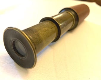 May include: A brass telescope with a brown leather covering on the end. The telescope is extended and the lens is visible.