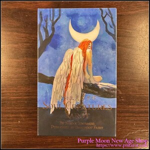 Puede incluir: Una caja de cartas de Tarot Soul Creatures con una ilustración de acuarela de una mujer alada sentada en una rama bajo una luna creciente. La caja es negra con letras doradas y el texto "Soul Creatures Tarot" y "Por Nawan Juntasiri Publicado por Barefoot Fairy".