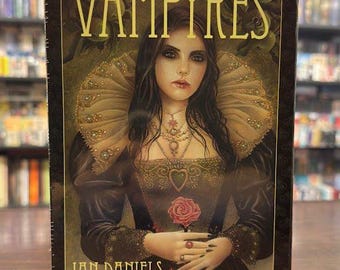 以下が含まれることがあります： 「The Tarot of Vampyres」タロットデッキの箱には、黒い髪と白い肌をした女性が描かれています。彼女は、大きな装飾的な襟が付いた黒いドレスを着ています。彼女は赤いバラを持っており、真剣な表情をしています。箱には金色の文字で「The Tarot of Vampyres」と書いてあります。
